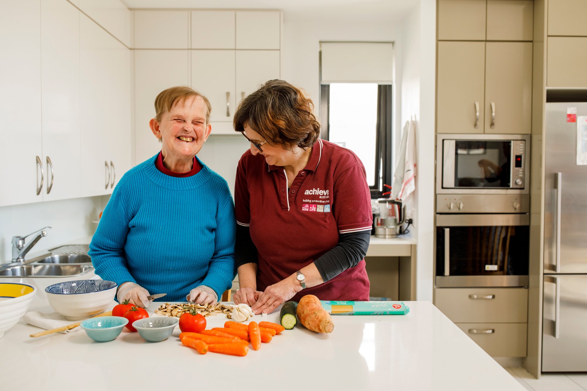 Woman with disability wearing a blue top chopping up vegetables at home with her support worker
