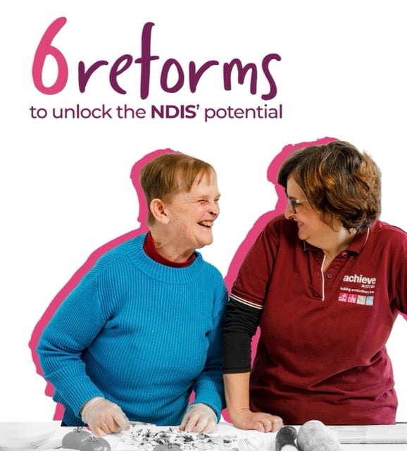 Graphic with the headline “6 reforms to unlock the NDIS’ potential” in bold lettering. Below the text, two people are engaged in an activity at a table covered with craft materials. One person is wearing a bright blue sweater, and the other is wearing a maroon Achieve Australia polo shirt with the logo and tagline visible. The background is white with a pink outline accentuating the figures.