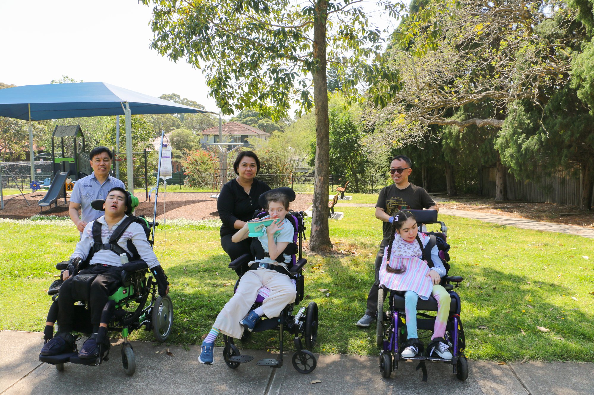3 people in wheelchairs at the park with 3 support workers