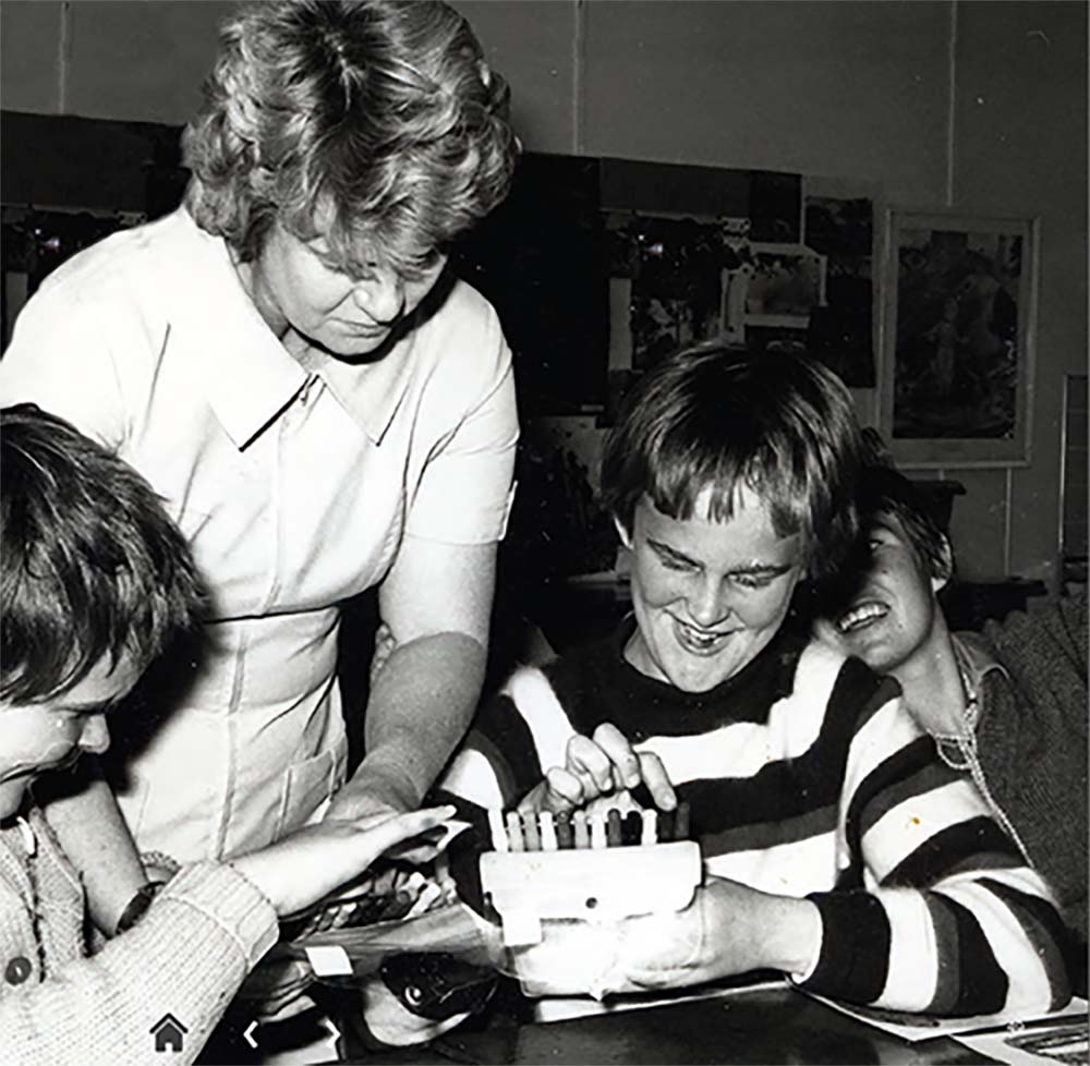 Black and white photo of a teacher leaning over two school aged boys